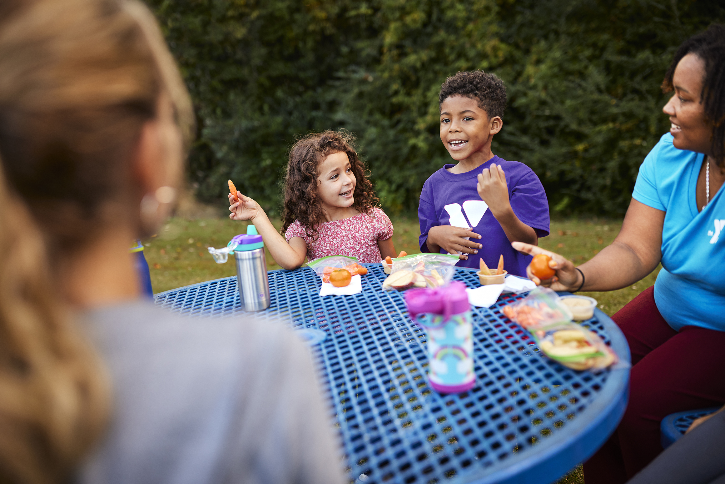 Kids and YMCA staff eating lunch at a picnic table Kids and YMCA staff eating lunch at a picnic table