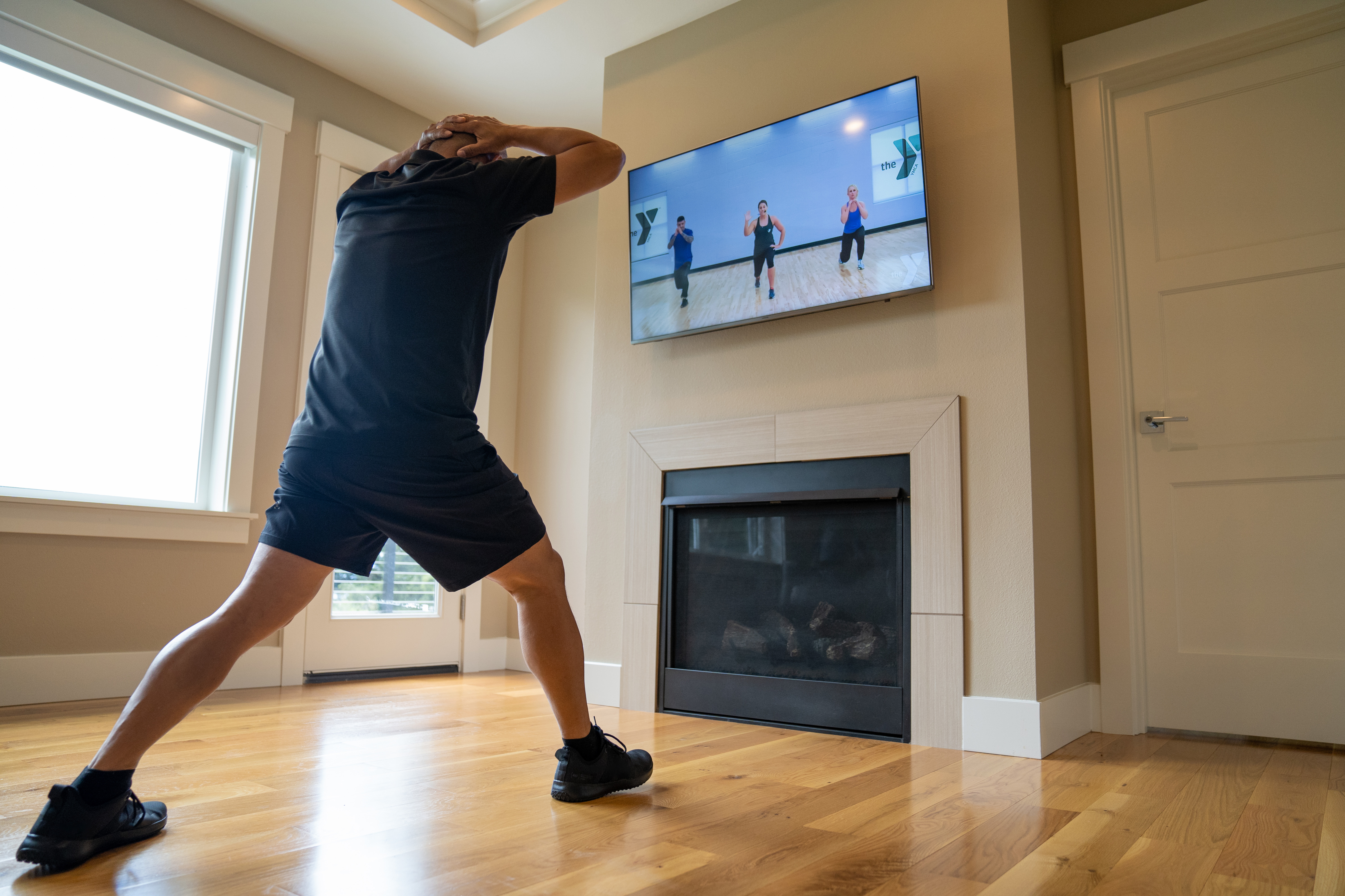Adult lunging as he works out during a YMCA Louisville virtual class playing on a TV screen. Adult lunging as he works out during a YMCA Louisville virtual class playing on a TV screen.