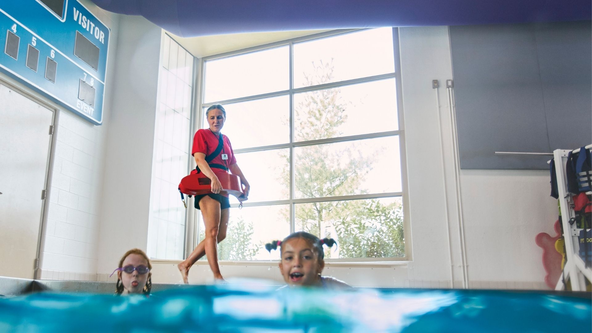 Older female lifeguard walking on pool deck watching children in pool Older female lifeguard walking on pool deck watching children in pool