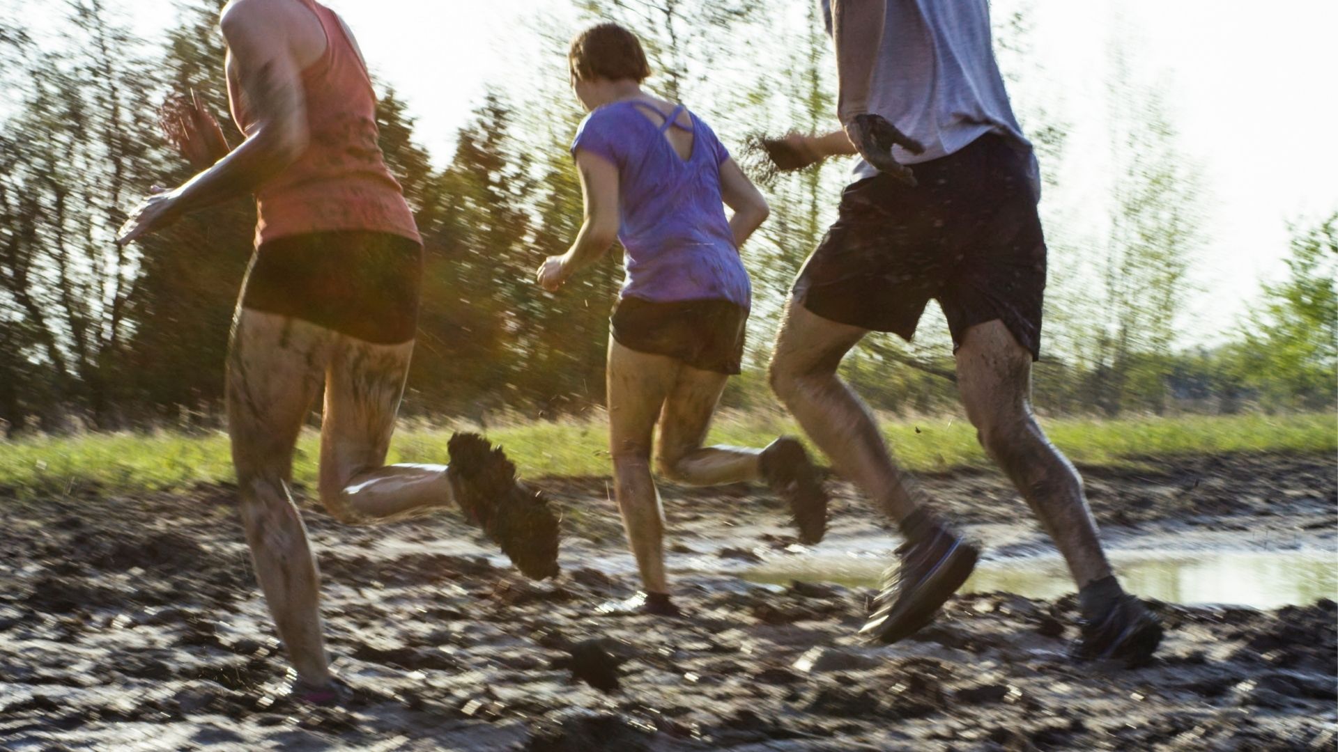 2 women and a man running through mud 2 women and a man running through mud