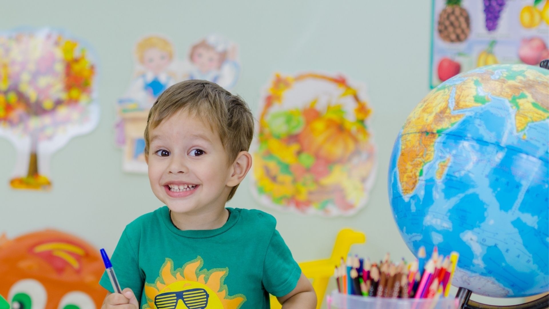 Smiling young boy sitting at table with art supplies and globe Smiling young boy sitting at table with art supplies and globe