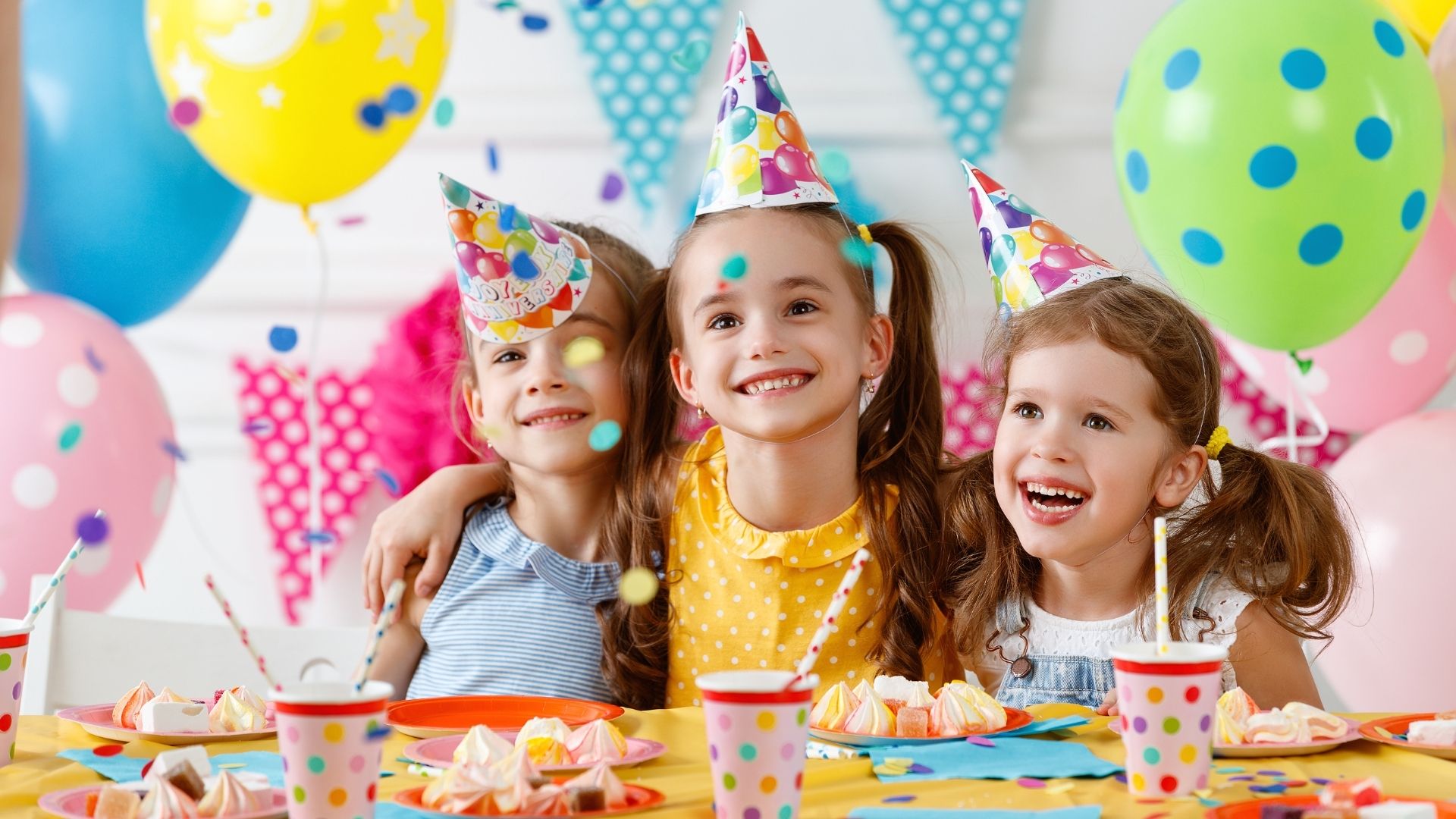 3 young girls in party hats smiling with balloons in the background 3 young girls in party hats smiling with balloons in the background