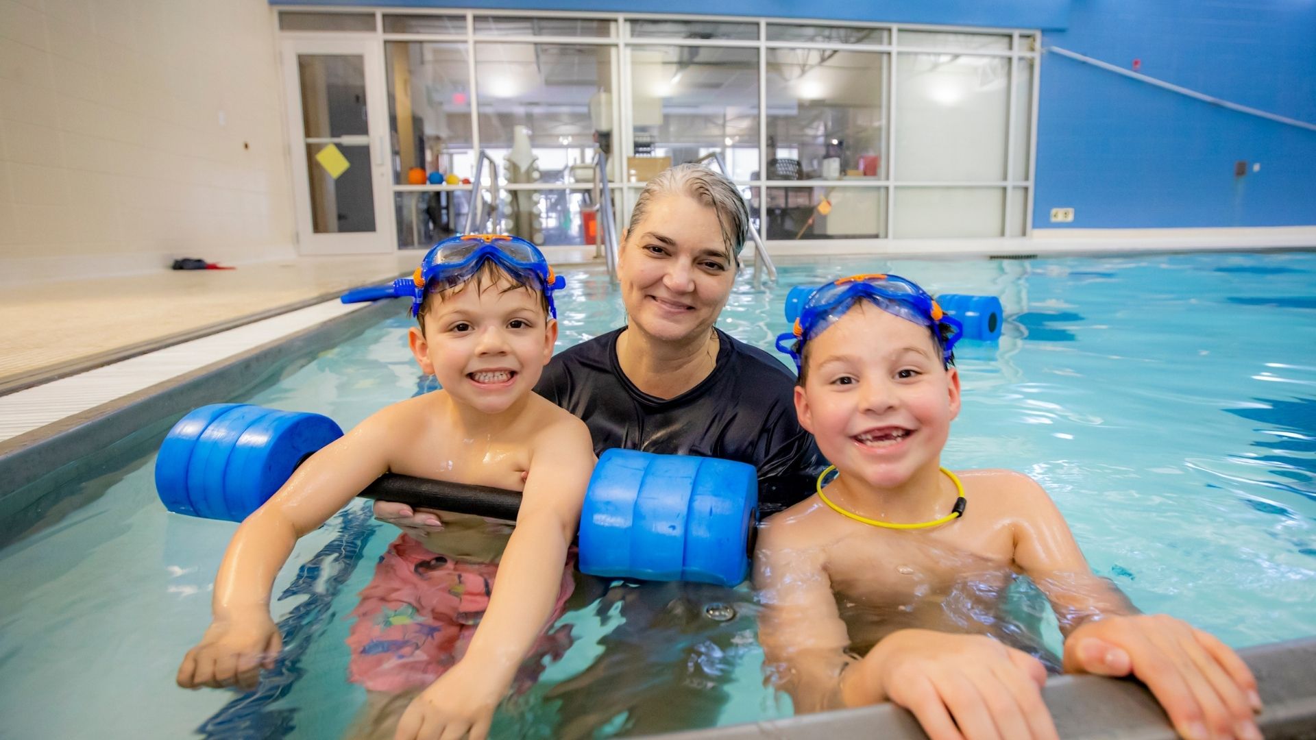 Swim instructor in pool with two smiling young boys Swim instructor in pool with two smiling young boys