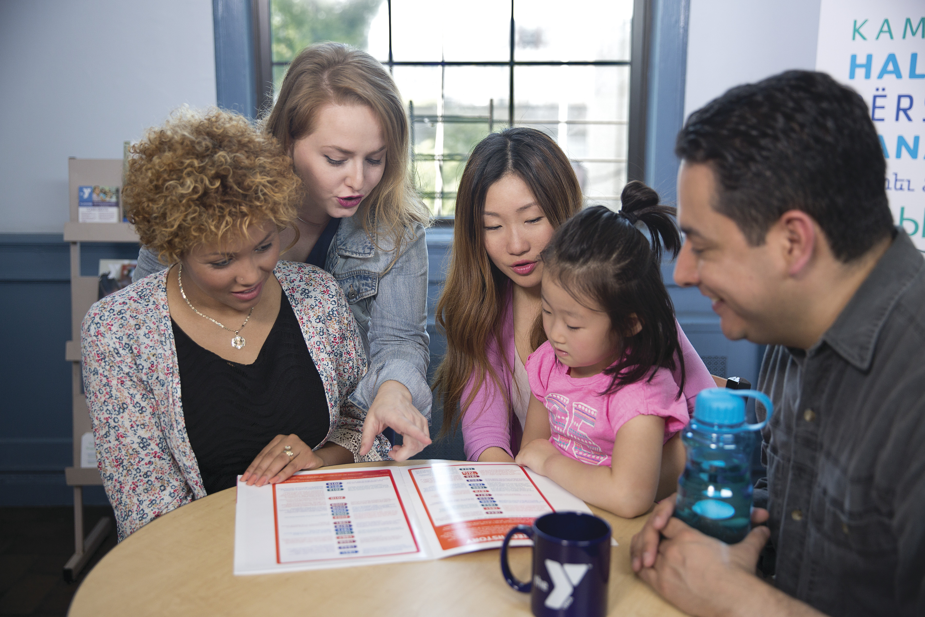 Four adults and one child reading through pamphlet on table Four adults and one child reading through pamphlet on table