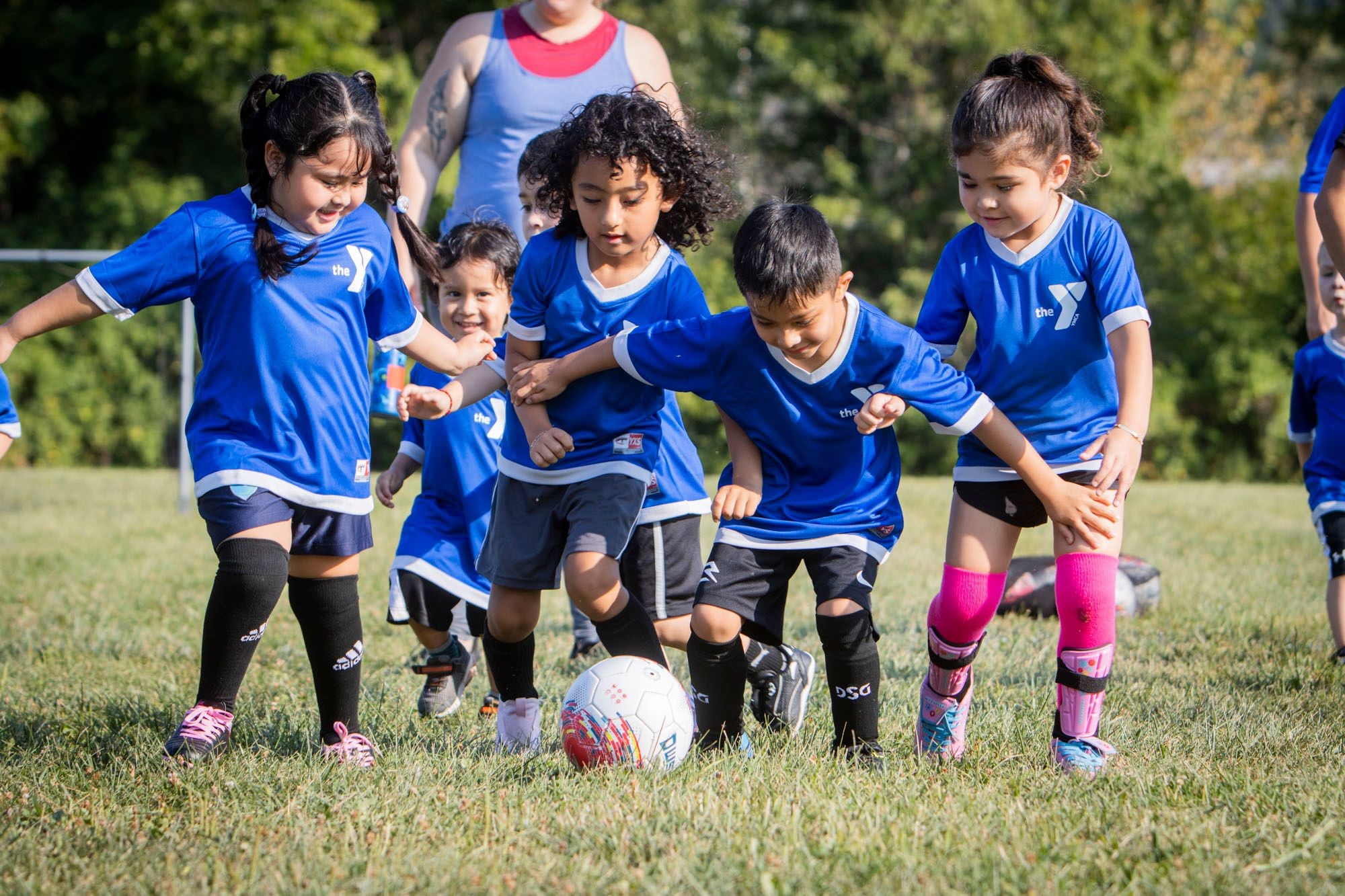 Group of children wearing YMCA soccer uniforms running after soccer ball Group of children wearing YMCA soccer uniforms running after soccer ball