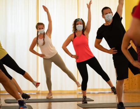 Adults in masks stretching in group fitness cardio class Adults in masks stretching in group fitness cardio class