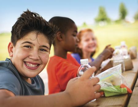 Smiling boy at picnic table with friends eating a healthy snack Smiling boy at picnic table with friends eating a healthy snack