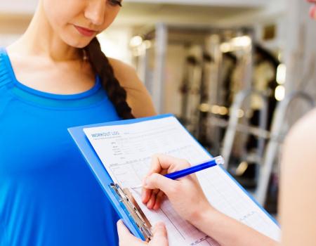 Trainer writing notes on clipboard as woman reads along Trainer writing notes on clipboard as woman reads along