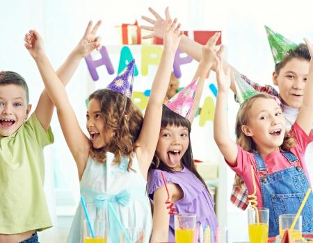 Group of kids in party hats with hands raised celebrating a birthday Group of kids in party hats with hands raised celebrating a birthday